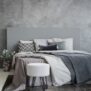 Striped carpet and stool in grey bedroom interior with sheets on bed with headboard. Real photo